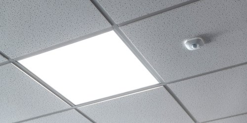 Detailaufnahme einer abgehängten Decke aus quadratischen Panels zeigt einen Sensor neben einer Einbauleuchte in Quadrat-Form.