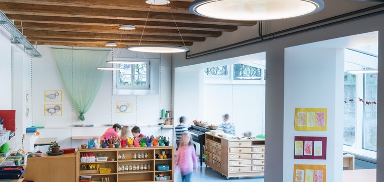 Große runde Pendelleuchten, die an einer Holzdecke angebracht sind, geben den Vorschulkindern in jeder Situation genügend Helligkeit.