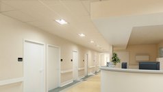 Ein in hellen Farben gehaltener Flur mit einer Rezeption bekommt durch das ausgewogene Licht von Deckeneinbauleuchten eine freundliche Atmosphäre.