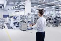 Im Vordergrund einer Produktionshalle ist ein Mitarbeiter zu sehen, der ein Tablet zur Lichtsteuerung bedient.