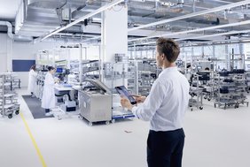 Im Vordergrund einer Produktionshalle ist ein Mitarbeiter zu sehen, der ein Tablet zur Lichtsteuerung bedient.