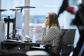 Eine Büroangestellte an ihrem Computerarbeitsplatz schaut auf den Bildschirm. Eine zusätzliche Tischleuchte erhellt ihren Schreibtisch.                                      