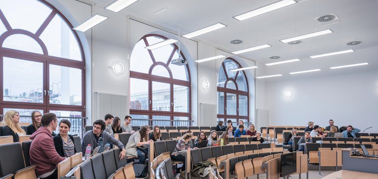 Große bodentiefe Fenster lassen viel Tageslicht in den Höhrsaal. Längs zu ihnen sind Pendelleuchten montiert, die eine blend- und schattenfreie Atmospäre schaffen. Wandleuchten ergänzen die Allgemeinbeleuchtung.