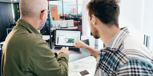 Zwei von hinten zu sehende Männer diskutieren die Konfiguration einer Lichtsteuerung, die auf dem Display eines Notebooks abgebildet ist.