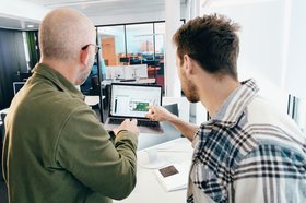 Zwei von hinten zu sehende Männer diskutieren die Konfiguration einer Lichtsteuerung, die auf dem Display eines Notebooks abgebildet ist.