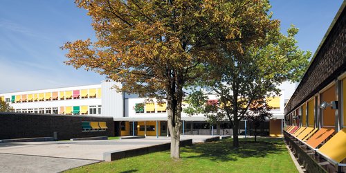 Der überdachte Eingangsbereich einer Schule ist mit runden Deckenanbauleuchten ausgestattet. 